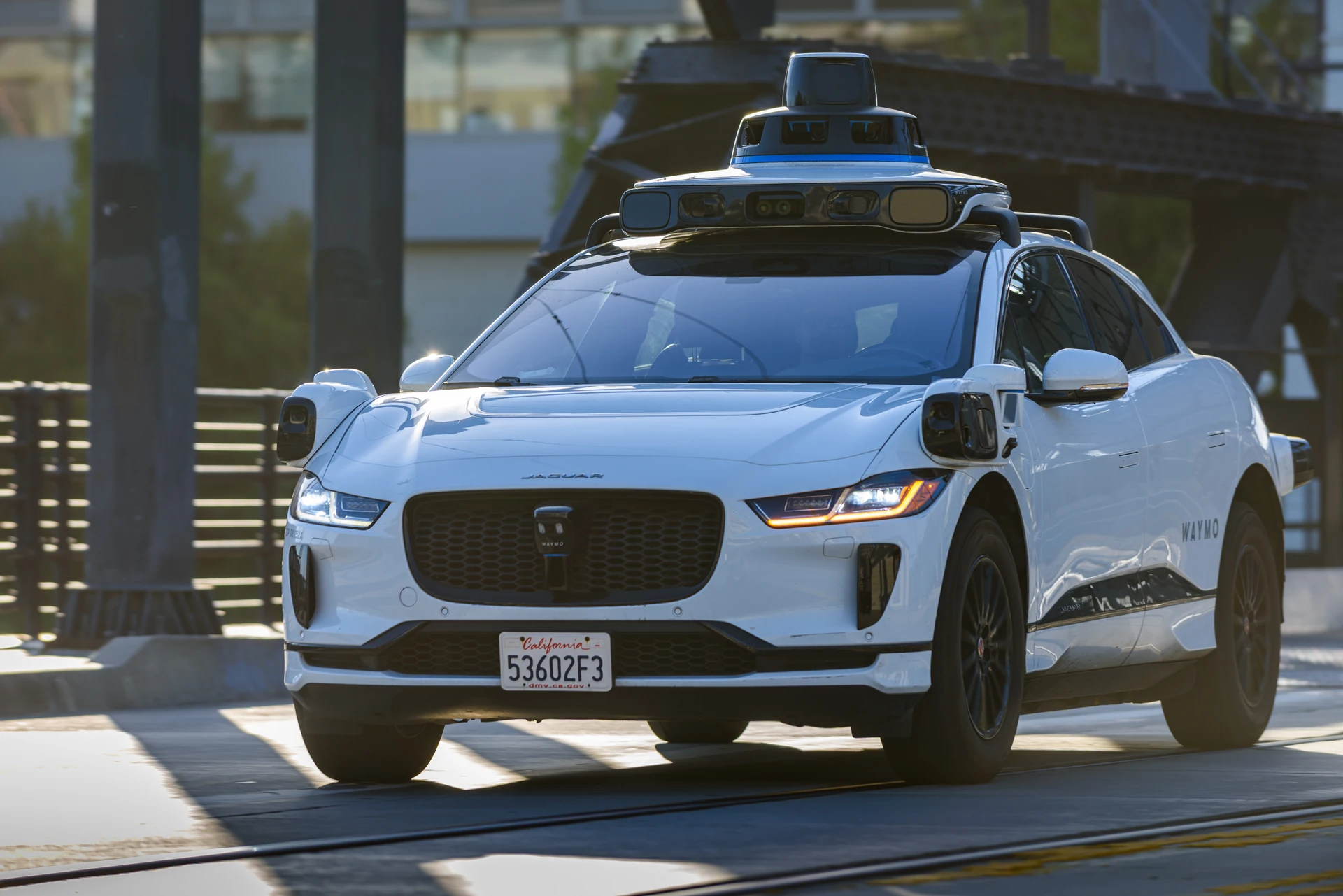 A Waymo Jaguar I-Pace with roof-mounted sensors driving on a city street