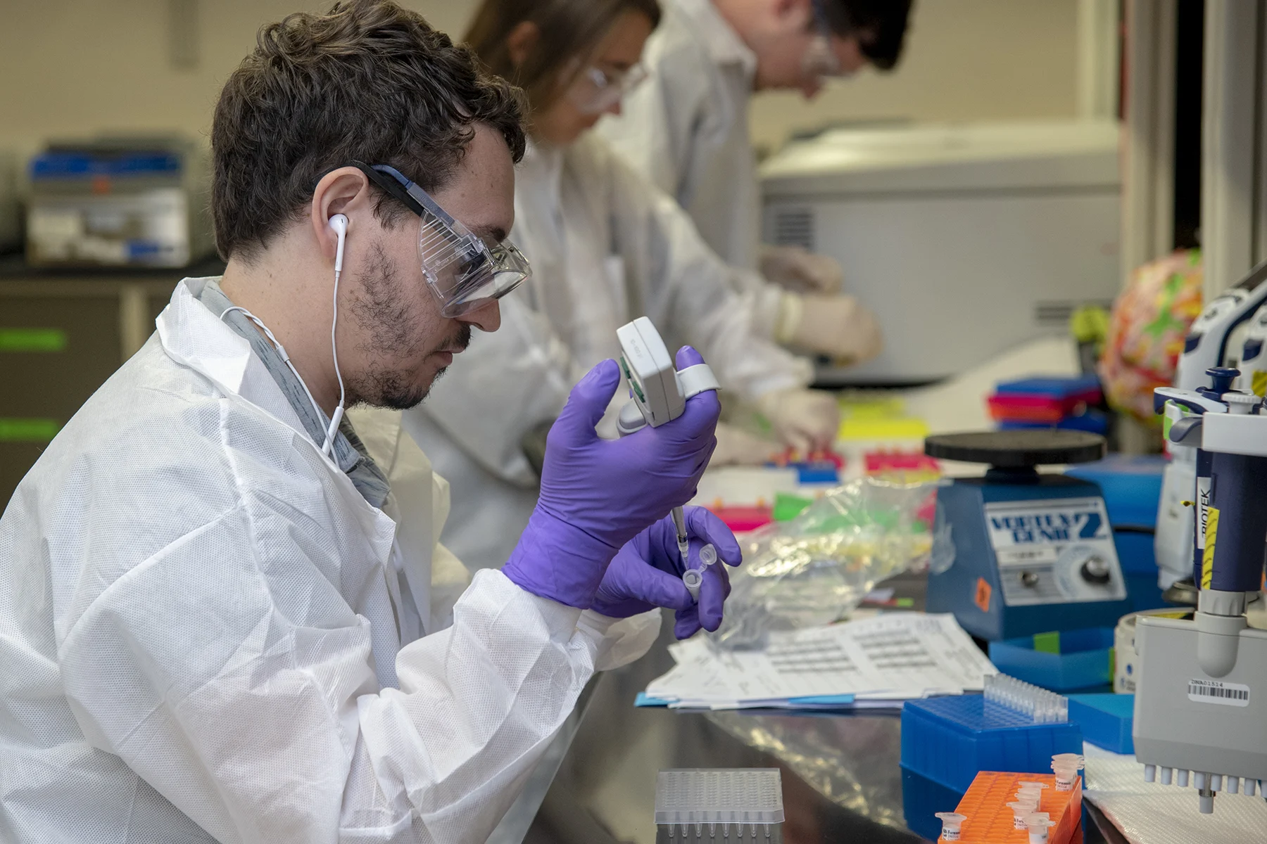DNA laboratory analysts in protective clothing prepare samples at a bench.