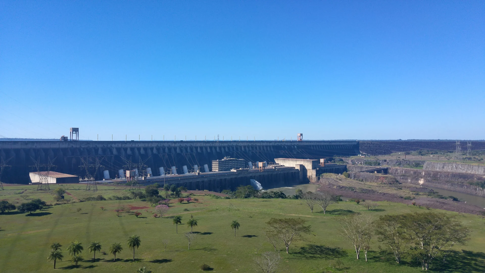 Itaipú Dam and its power station behind a grassy slope, photographed in August 2016.