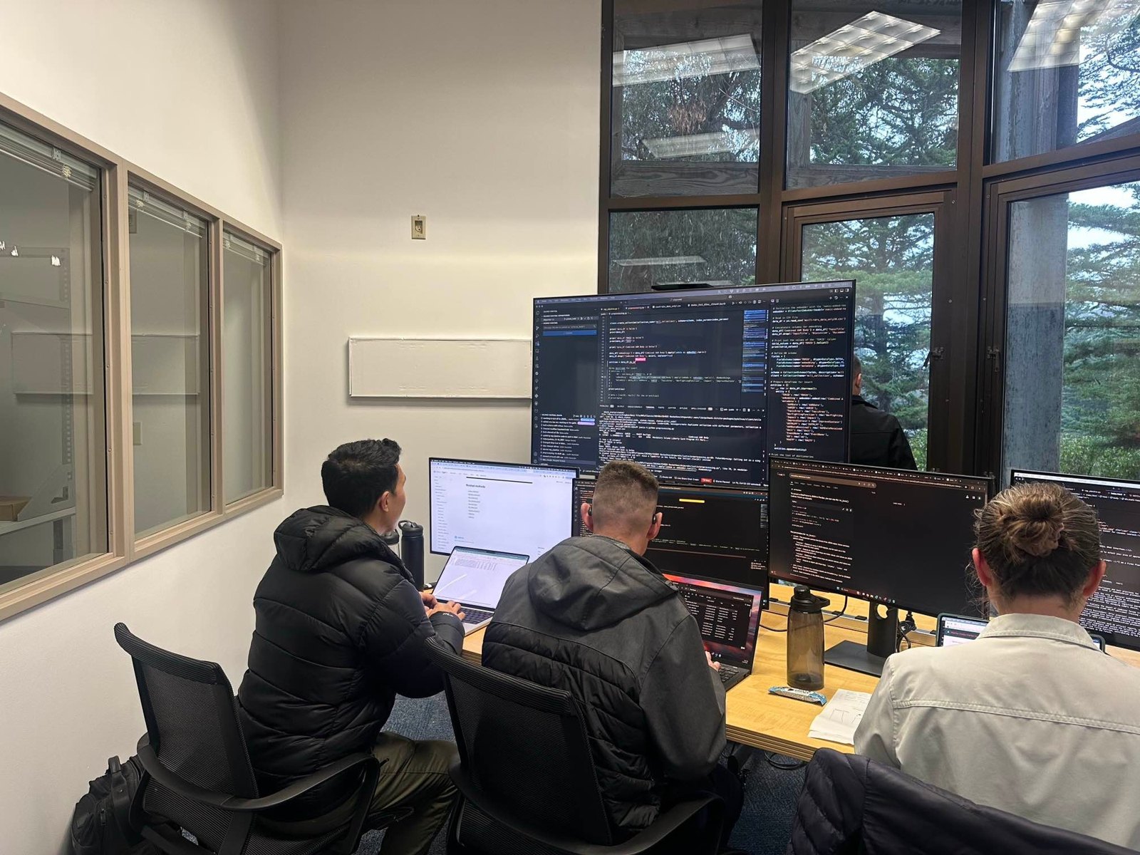 Three Naval Postgraduate School students work at computers during an AI hackathon