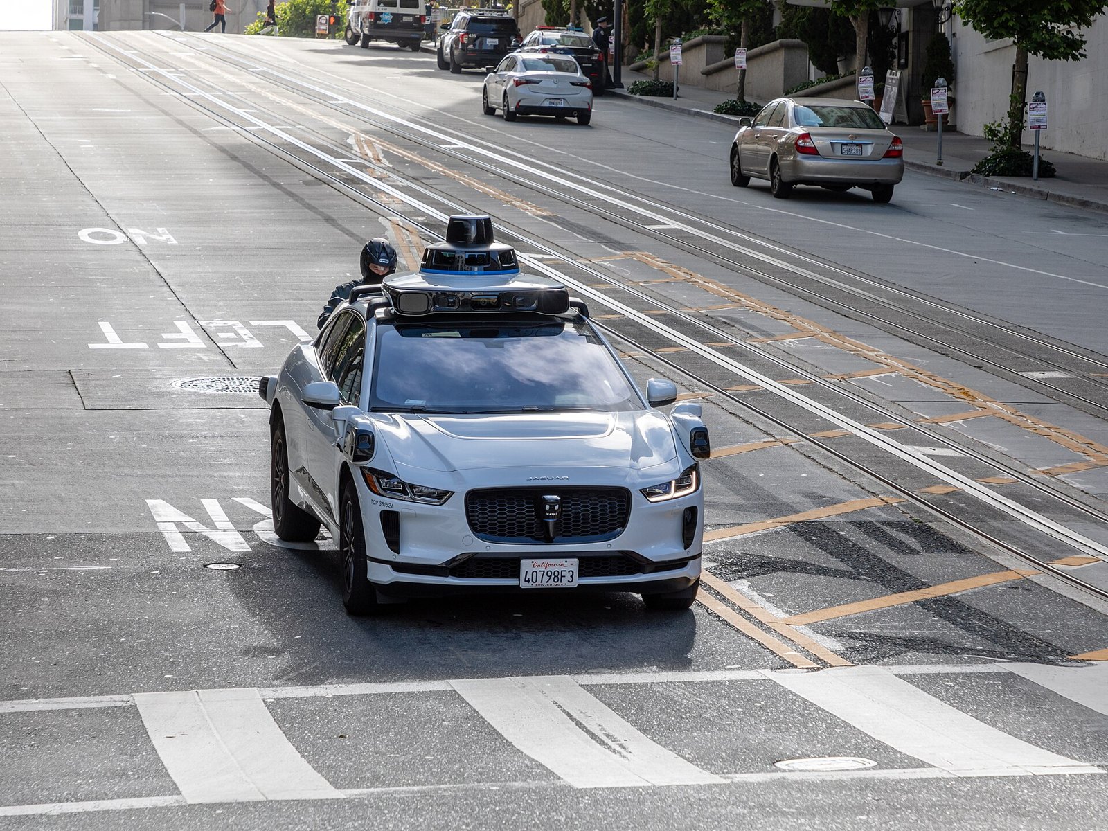A white Waymo vehicle with rooftop sensors traveling on a San Francisco street