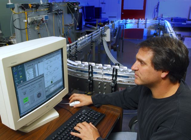 NIST engineer Joe Falco programs a controller beside a bottling-line testbed in an archival photograph from 2007.