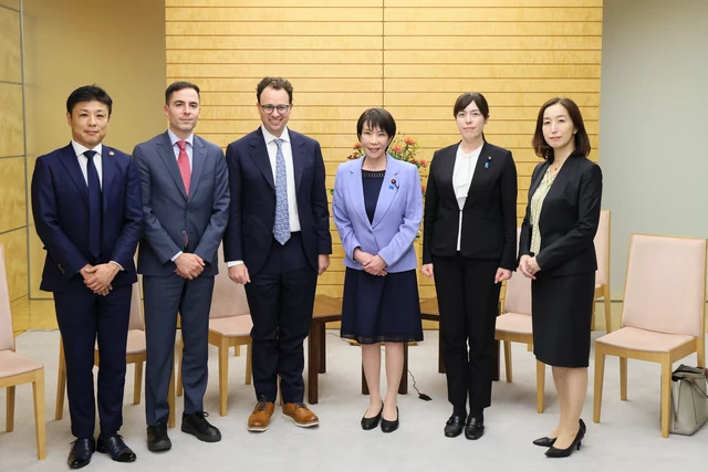 Dario Amodei in a navy suit and tie stands beside Sanae Takaichi for an official group photograph.
