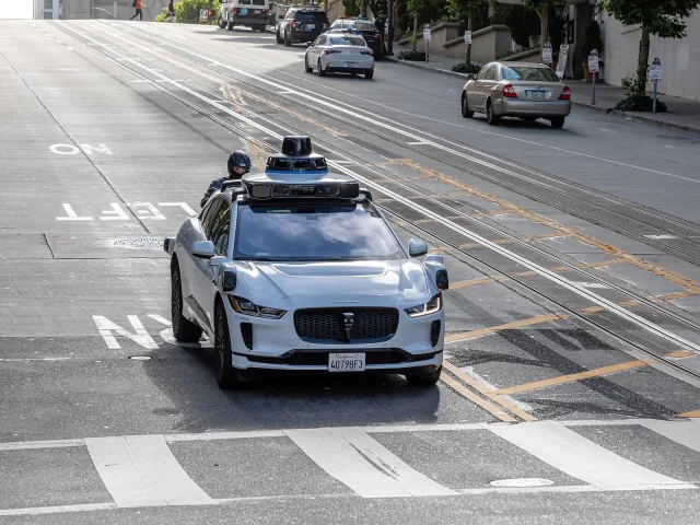 A white Waymo vehicle with rooftop sensors traveling on a San Francisco street