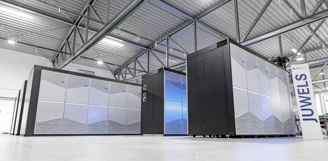 Rows of silver and black JUWELS Booster supercomputer cabinets inside a bright equipment hall.