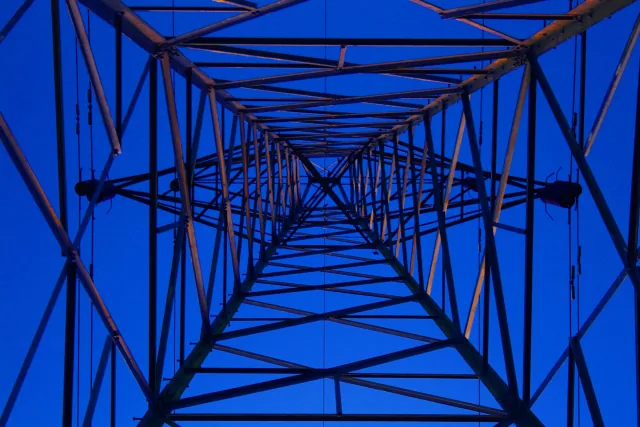 View upward through a steel electricity pylon against a blue evening sky.