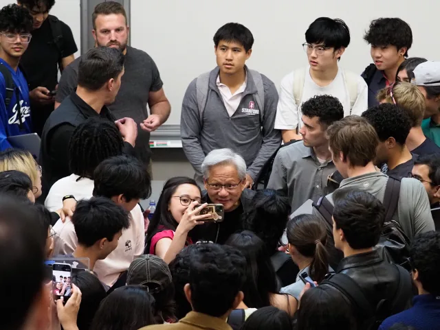 Jensen Huang poses for a selfie among students crowded around him at Stanford University.