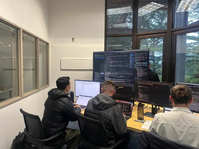 Three Naval Postgraduate School students work at computers during an AI hackathon